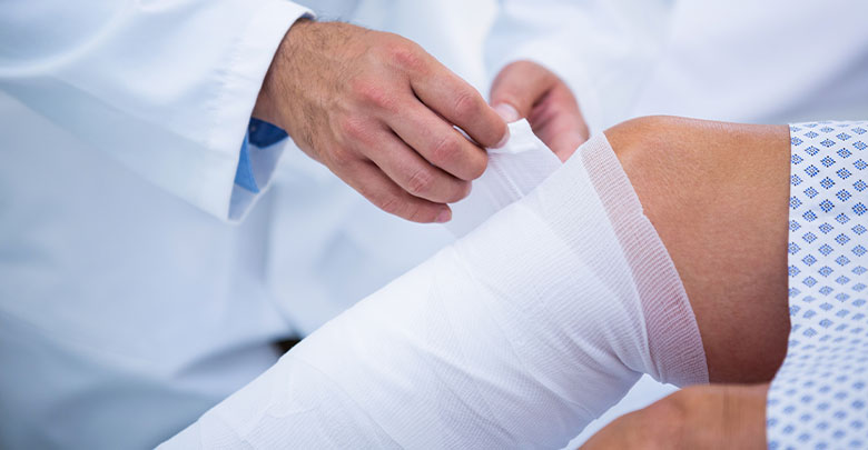 The doctor or nurse is wrapping the patients knee in a bandage following surgery for knee replacement 