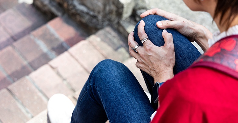 A middle aged woman holds her knee, and she wonders what the causes and symptoms of osteoarthritis are. 