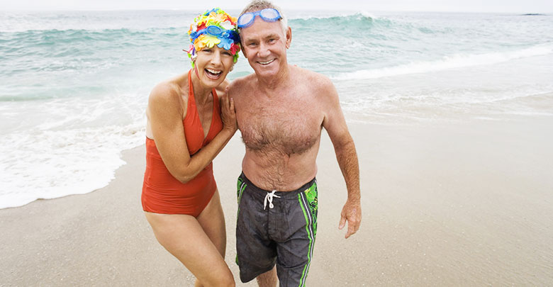 An older couple in fun swimsuits enjoy swimming in the ocean for their arthritis and pain.