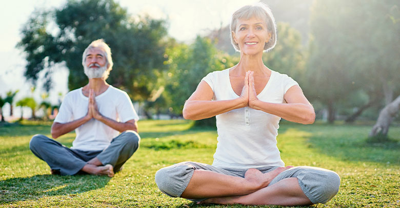 Yoga for arthritis is very beneficial. An older woman and man are sitting outdoors in nature and benefitting from yoga for their arthritis.