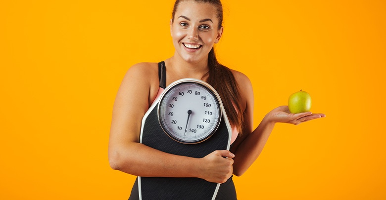 Attractive healthy young woman motivating you to lose weight, holding a scale and an apple. 