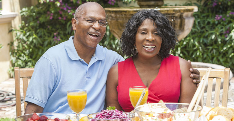 A laughing couple enjoy a healthy meal together outside.