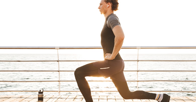 Young athletic man doing a lunge as a torn meniscus exercise on a seaside promenade